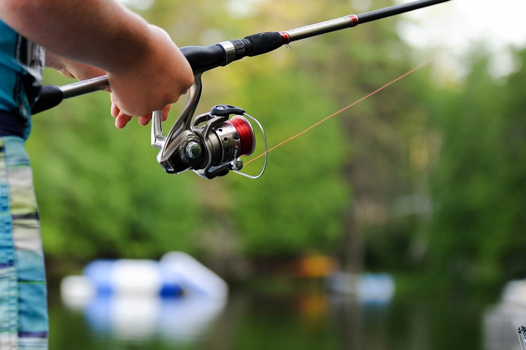 A serene lake scene with a fisherman wearing a life jacket, holding fishing gear, and a boat in the background, emphasizing safety while fishing.